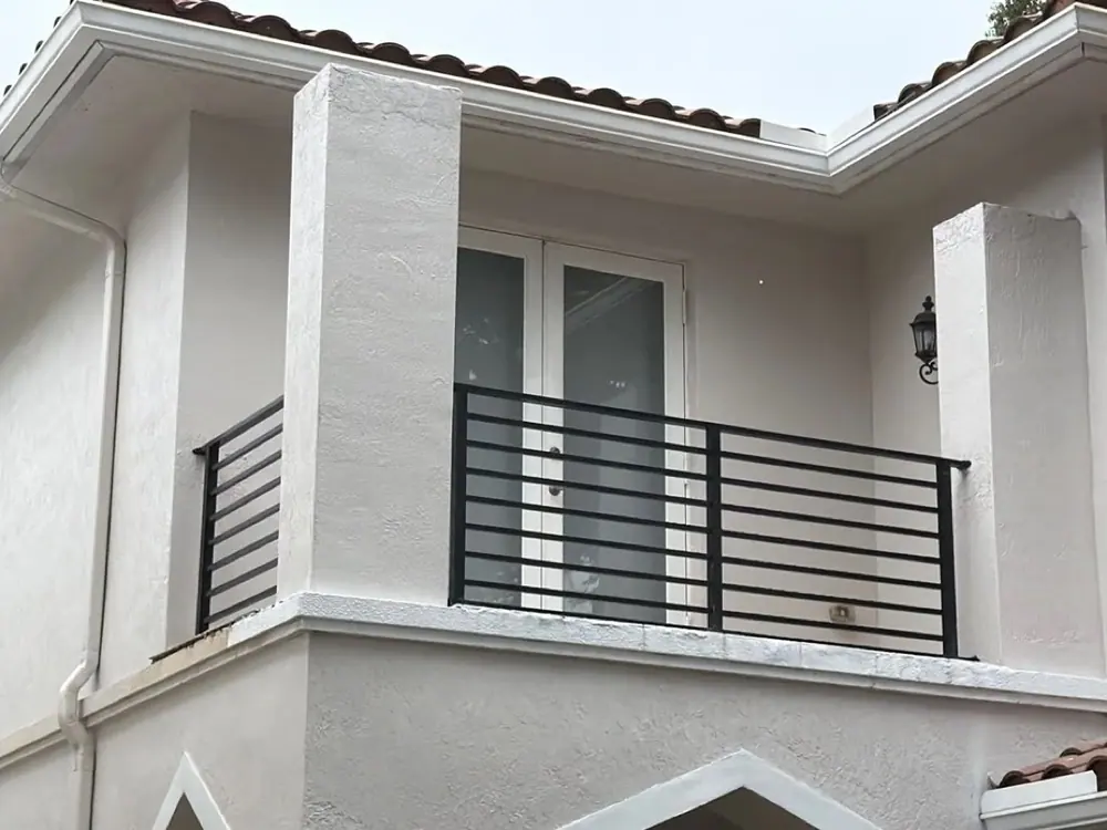 Finished stucco balcony with a black horizontal railing and white French doors