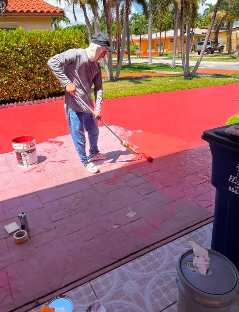Exterior painting: painter rolling a bright red coating onto a driveway